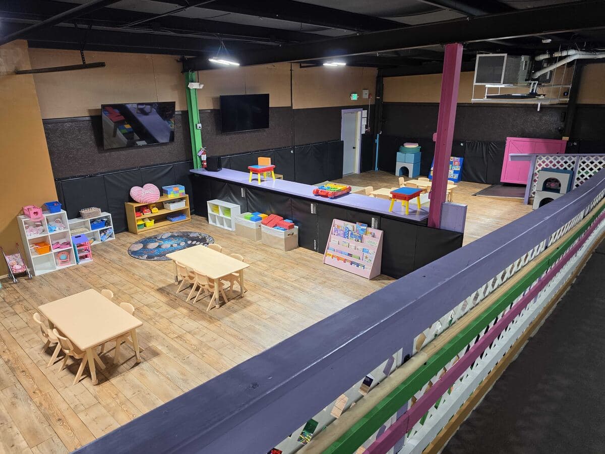 Upstairs room with child-size tables, play shelves and wall-mounted TVs