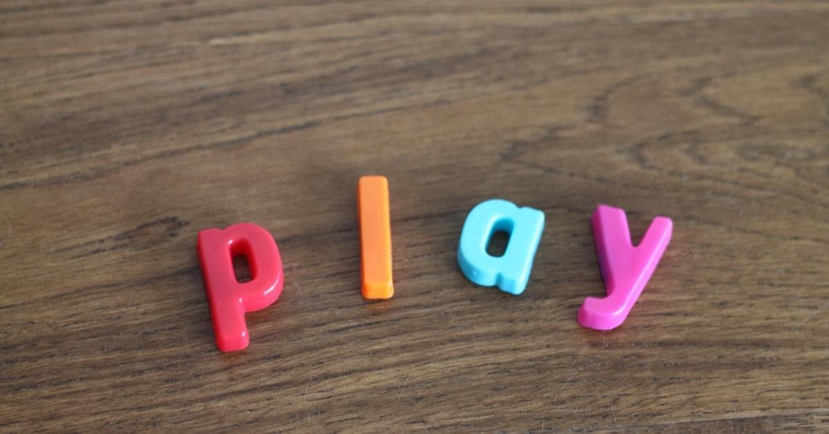 Colorful letters spelling ‘play’ laid out on a wooden surface.